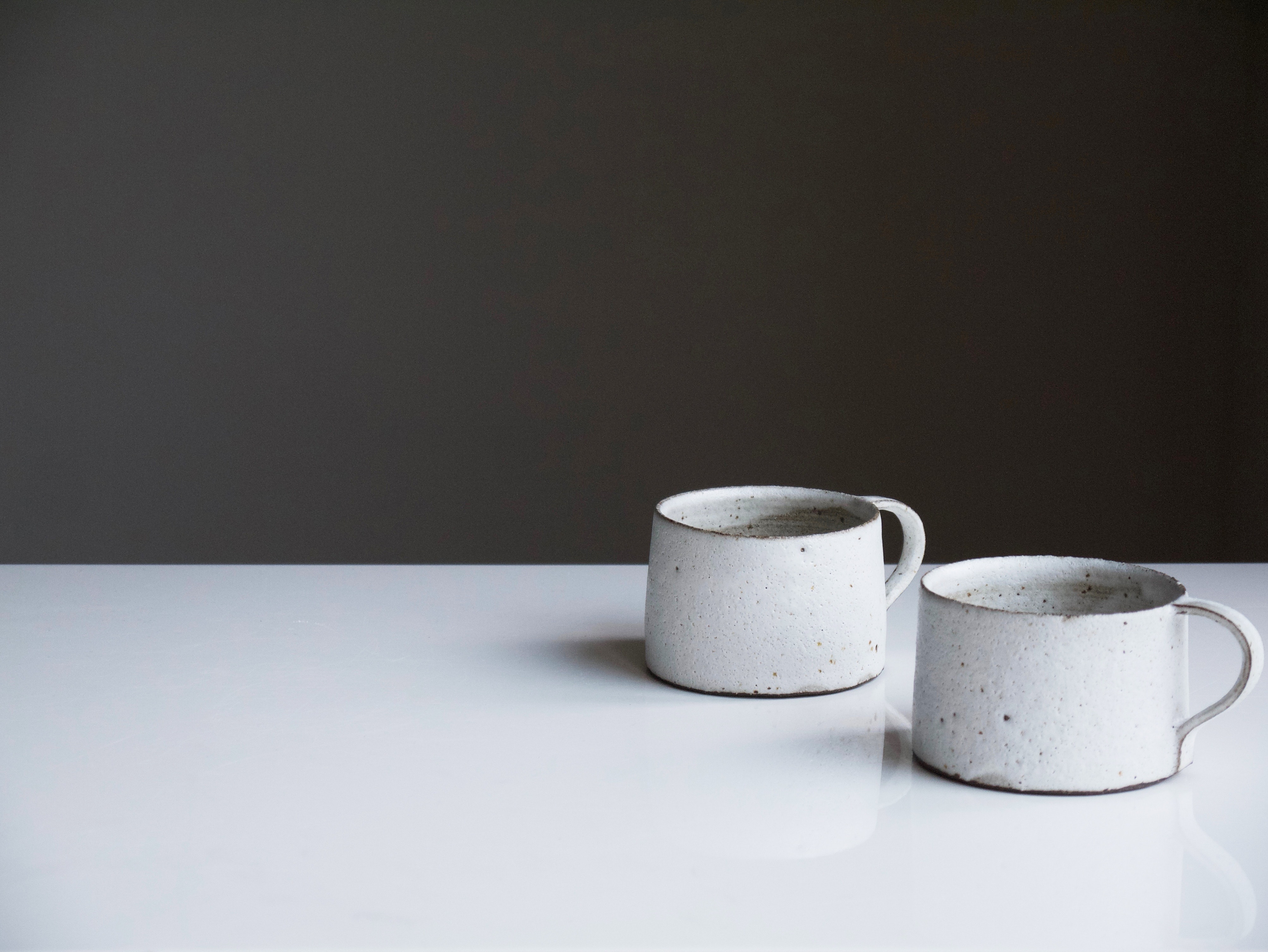 Two ceramic mugs sit on a white table