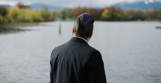 Matsui looks out onto a small body of water. We see the back of their head.