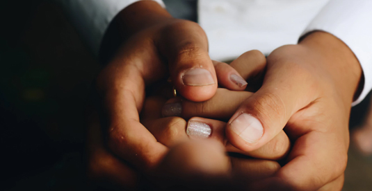 A close cropped image of a person gently holding another person's hands.